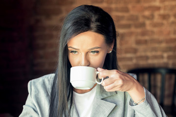 Young businesswoman is drinking coffee wearing jacket in cafe.