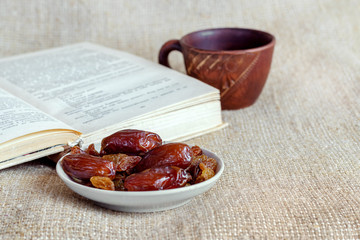 A plate of dates and raisins near a cup of coffee and an open book
