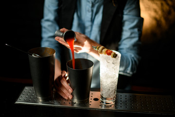 Fototapeta na wymiar woman bartender gently pours drink from jigger into metal glass