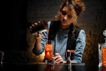 female bartender pours tomato juice into glass with ice.