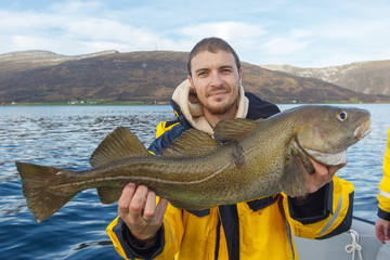 Happy fisherman with cod fish in hands