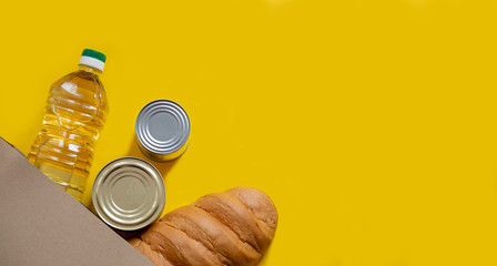 A loaf of bread, sunflower oil and canned food in a paper bag on a yellow isolated background. Food...
