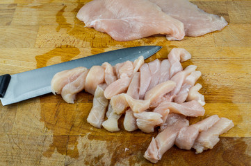 Fototapeta na wymiar Chopped raw chicken breasts and knife on a wooden chopping board