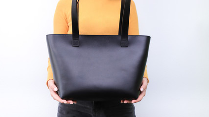 Handmade black leather women's handbag in the hands of a young girl in a yellow sweater