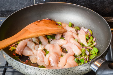 Cooking sliced onions, green peppers and chicken breasts on a frying pan close up.