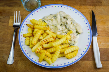 Ready to eat sliced chicken with onions and peppers in a cooking cream sauce with french fries on a dish.