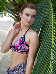 Beautiful young woman in bikini standing near palm leaves.