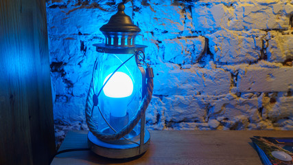 Vintage table lamp shines blue light on brick wall background.