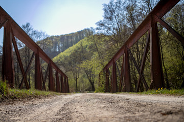An iron rusty old vintage footbridge with dirt road in a green forest