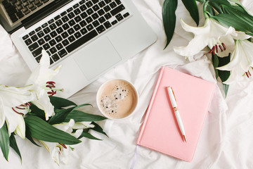 Morning bed with notebook, laptop, coffee cup and flowers on the white bed sheet. Good morning and...