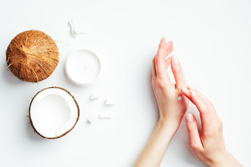 Female hands applying coconut cream on white background. Coconut organic cosmetics, oil, lotion for...