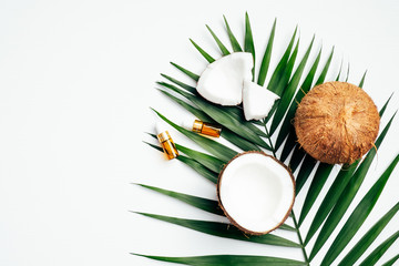 Obraz na płótnie Canvas Natural coconut oil for hair, SPA organic cosmetic concept. Flat lay, top view tropical palm leaf, coconuts, essential oil bottles on white background.
