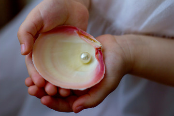 Children's hands hold oyster shell with pearls