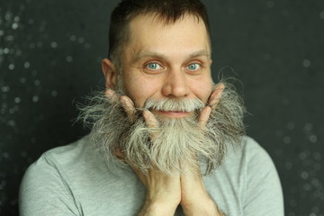 Studio portrait of a bearded middle-aged man in a gray t-shirt, he looks at the camera, smiling,...