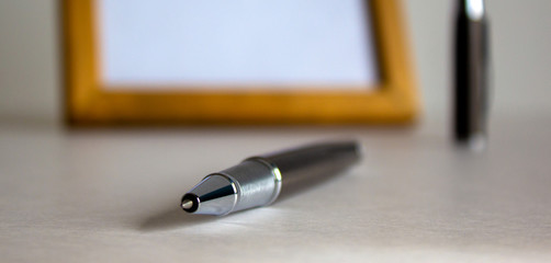Notebook and pen on beautiful white fon. Wooden picture frame and cap in the background.