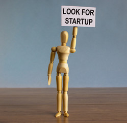 Wooden model of a man holding a tablet saying 'look for startup'.