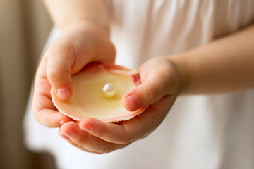 Children's hands hold oyster shell with pearls