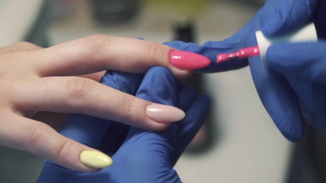Paints female nails with pink gel polish in blue protective gloves