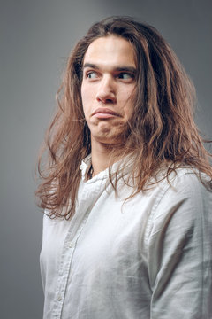 Funny guy with surprised expression. Comic cheerful young man with long hair on isolated background in studio
