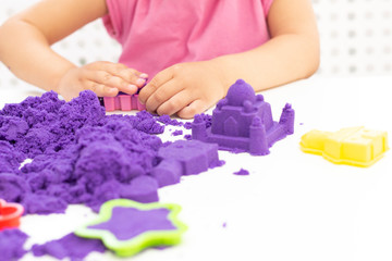 Fototapeta na wymiar Childrens hands plays kinetic sand in quarantine. purple sand on a white table. coronavirus pandemic