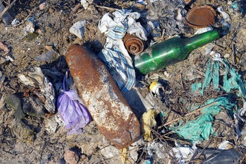 a pile of garbage from a green glass bottle with rusty cans and pieces of colored cloth in a...
