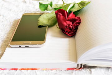 On the notebook is a faded red rose and a smartphone.