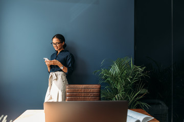 Young woman using a cell phone at a home office. Side view of a female entrepreneur working...