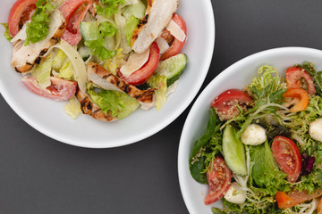 white deep plates with fresh salad ingredients mixed with sauce placed on an gray background. A place for a menu, banner or advertisement