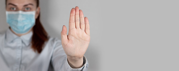 Paramedic in medical shows stop sign with hand on gray wall in clinic