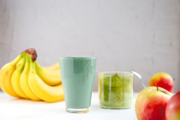 The concept of food and drink, diet and nutrition. Healthy green vegan smoothie with banana, spirulina and ripe apple for summer detoxification