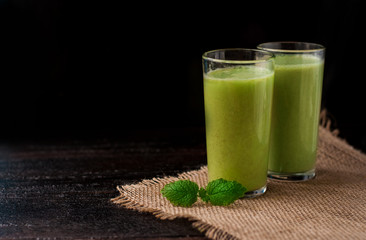 green refreshing smoothie of kiwi, Apple, avocado or banana with mint in two glasses. there's a mint leaf in front. Breakfast for two. banner, copyspace.
