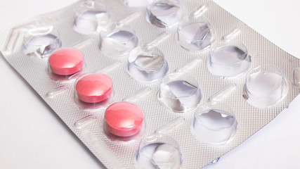 Three pink pills in pack on gray background