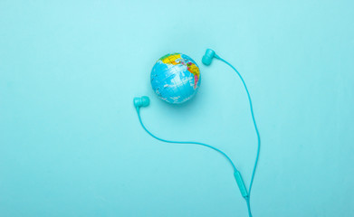 World song. Global music chart. The music of earth. Stereo earphones and a globe on a blue  background. Top view