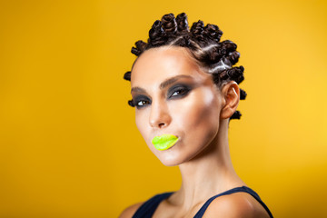portrait of a girl on a yellow background of Caucasian-Asian appearance with a creative hairstyle in the form of horns and yellow lips, stares intently at the camera