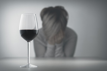 Glass with alcohol on blurred view of a lonely and desperate drunk woman