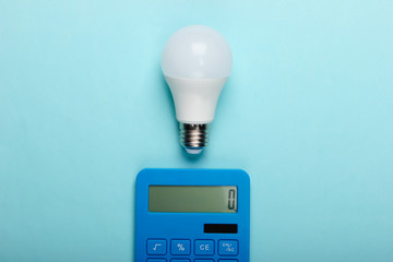 Energy saving. Calculator with led light bulb on a blue pastel background. Top view