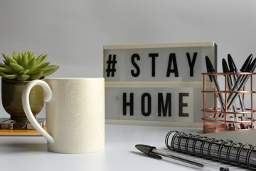 Home office desc with cup of coffee, stationary, home plant and Stay Home sign. Stay  home concept,  office desc concept during pandemic