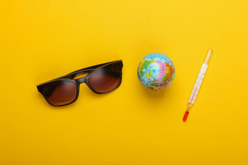 Flat lay summer background. Beach vacation. Globe with a thermometer, sunglasses on a yellow background. Global warming. Top view