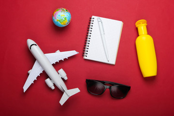 Planning Travel and beach vacation. Summer background. Airplane figurine, globe, sunglasses and sunblock, notebook on red background. Top view. Flat lay