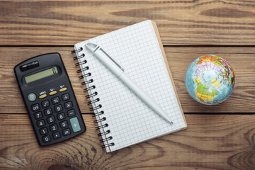 Calculator, globe and notebook on wooden table. Top view. Minimalism. Education concept, geography