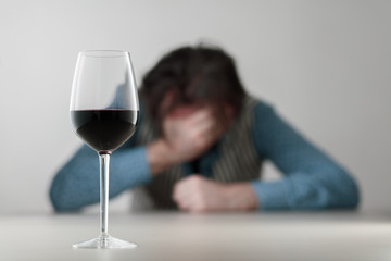 Glass with wine/ alcohol on blurred view of a lonely and desperate drunk man