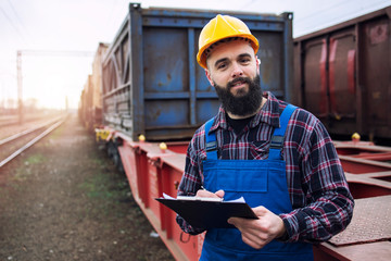 Portrait of shipping worker holding clipboard and dispatching cargo containers via railroad....