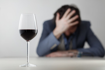Glass with wine/ alcohol on blurred view of a lonely and desperate drunk man