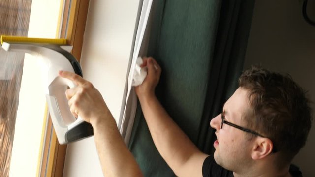 man washing the balcony window with a modern electric battery washer