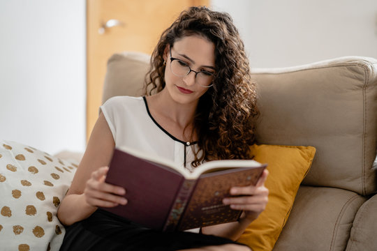 Mujer joven blanca leyendo un libro con inter&eacute;s desde casa