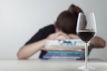 Glass with alcohol on blurred view of a lonely and desperate drunk woman lying on a stack of books .