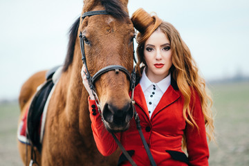 Obraz premium red-haired jockey girl in a red cardigan and black high boots with a horse
