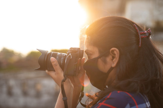 Back light portrait of an Indian young woman with corona preventive mask taking photographs on a rooftop in home isolation.Indian lifestyle, disease and home quarantine.