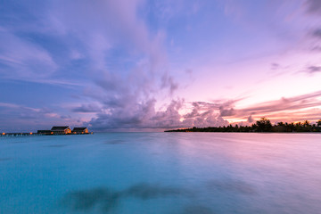 Amazing sunset sky and reflection on calm sea, Maldives beach landscape of luxury over water bungalows. Exotic scenery of summer vacation and holiday background
