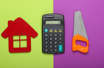 Calculation of the cost of building a house or repair. House figurine, calculator and toy saw on a green-purple background. Top view